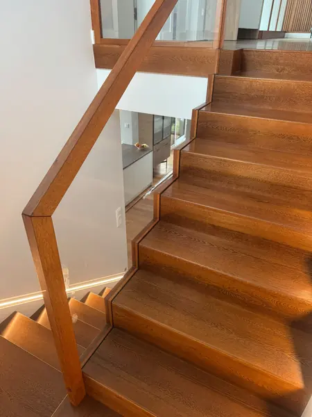 Drewniane schody z balustradą ze szkła i drewnianą poręczą