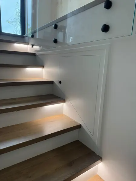 Drewniane stopnie przy ścianie z podświetleniem i balustradą ze szkła