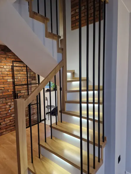 Podświetlone schody z balustradą z pionowych czarnych prętów aż do sufitu