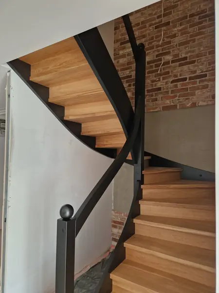 Dębowe schody zabiegowe z giętą stalową balustradą przy ścianie z cegły